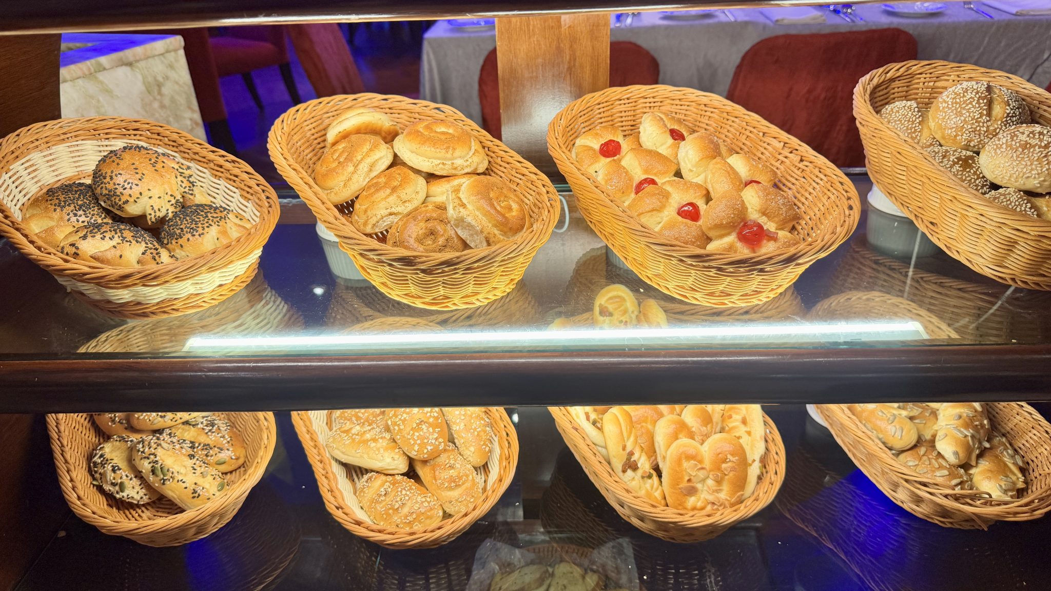 A bakery shelf of fresh bread rolls in baskets, by Faisal Ahammad