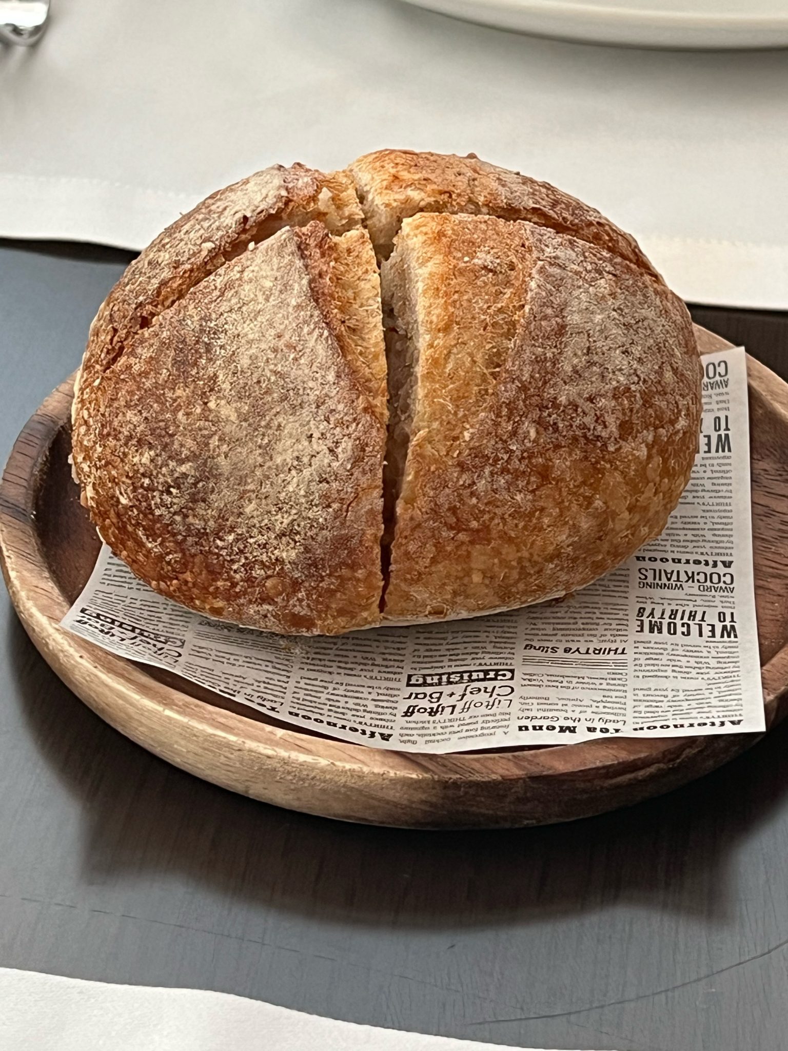 A round loaf with a cross cut into the crust, on a wooden plate, by Alina Kakshapati
